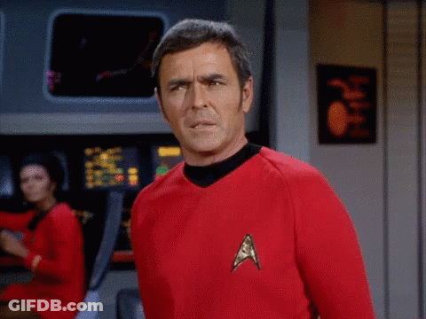 A Man In A Red Star Trek Uniform Stands In Front Of A Computer Screen GIF