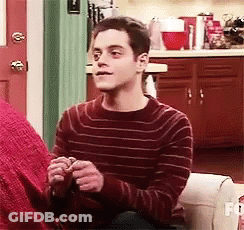 A Man In A Red Striped Sweater Is Sitting On A Couch Holding A Knitting Needles . GIF