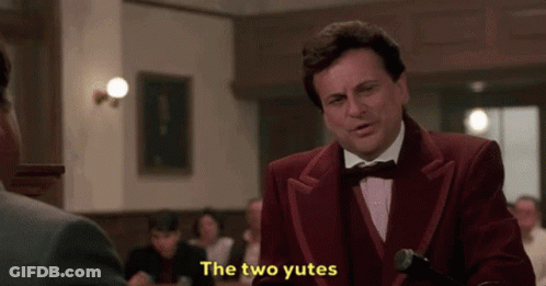 A Man In A Red Suit And Bow Tie Is Standing In Front Of A Microphone And Says The Two Yutes . GIF