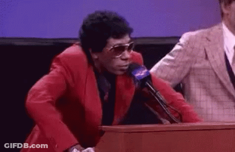 A Man In A Red Suit And Sunglasses Is Standing At A Podium . GIF