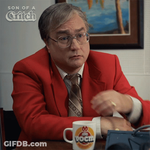 A Man In A Red Suit And Tie Is Sitting At A Table With A Cup That Says Boom GIF