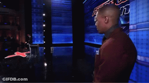 A Man In A Red Suit And Tie Stands In Front Of A Sign That Says America 'S Got Talent GIF