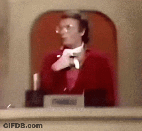 A Man In A Red Suit And White Tie Is Standing In Front Of A Glass Door . GIF