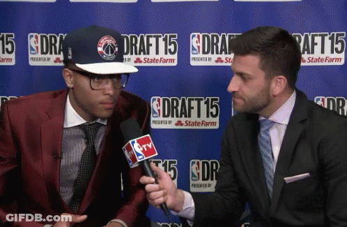 A Man In A Red Suit Is Being Interviewed By A Man In A Suit In Front Of A Sign That Says Draft 15 GIF