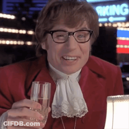 A Man In A Red Suit Is Holding A Glass Of Champagne And Smiling GIF