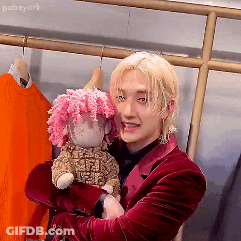 A Man In A Red Suit Is Holding A Stuffed Sheep With Pink Hair . GIF