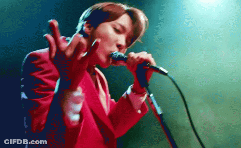 A Man In A Red Suit Is Singing Into A Microphone GIF