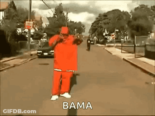 A Man In A Red Suit Is Walking Down A Street With The Word Bama On The Bottom . GIF