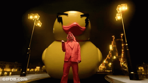 A Man In A Red Suit Stands In Front Of A Giant Yellow Rubber Duck GIF