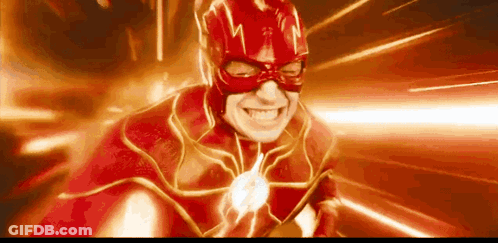 A Man In A Red Superhero Costume Is Smiling With A Flash Coming Out Of His Mouth . GIF