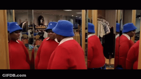 A Man In A Red Sweater And Blue Hat Looks At Himself In The Mirror GIF