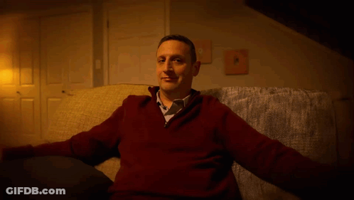 A Man In A Red Sweater And Tie Is Sitting On A Couch GIF