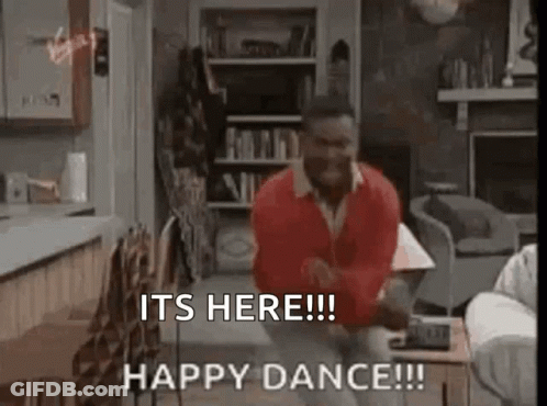 A Man In A Red Sweater Is Dancing In A Living Room With The Words `` It 'S Here ! '' GIF