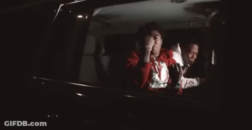 A Man In A Red Sweater Is Sitting In The Back Seat Of A Car . GIF