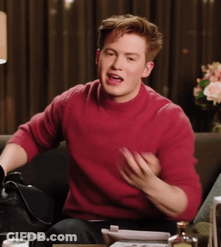 A Man In A Red Sweater Is Sitting On A Couch And Talking GIF