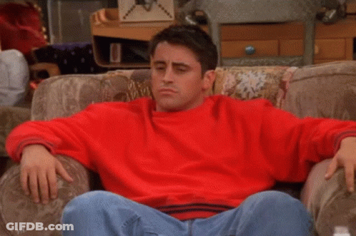 A Man In A Red Sweater Is Sitting On A Couch With The Words Ah-Ha Written On His Chest . GIF