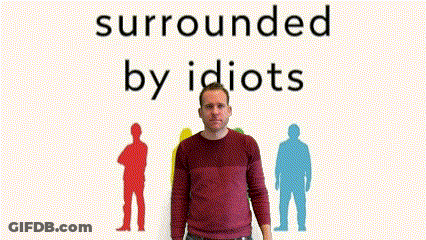A Man In A Red Sweater Is Standing In Front Of A Sign That Says Surrounded By Idiots GIF