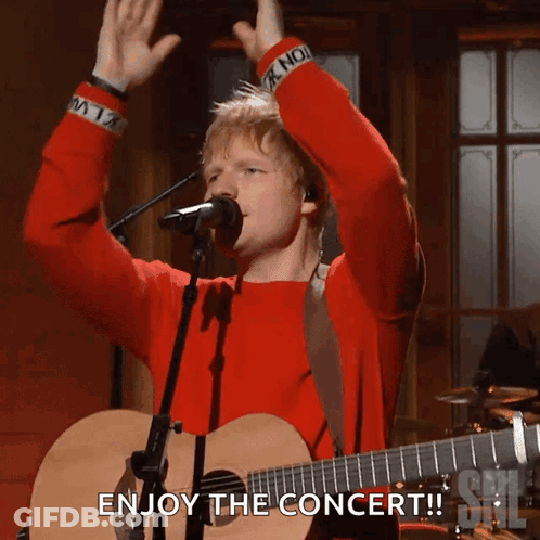A Man In A Red Sweater Singing Into A Microphone With The Words Enjoy The Concert GIF