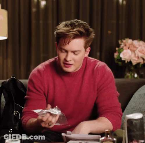 A Man In A Red Sweater Sits At A Table GIF