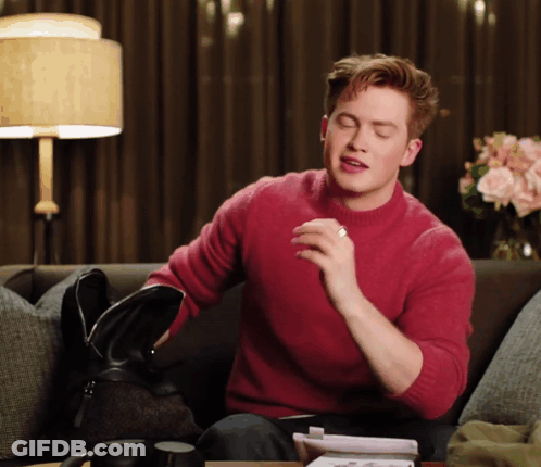 A Man In A Red Sweater Sits On A Couch Holding A Black Bag GIF