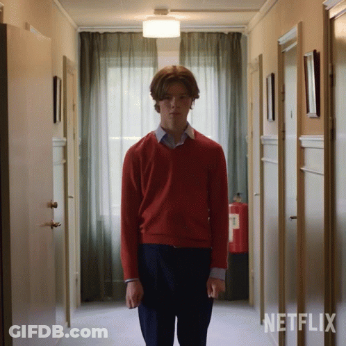 A Man In A Red Sweater Stands In A Hallway With Netflix Written On The Wall Behind Him GIF