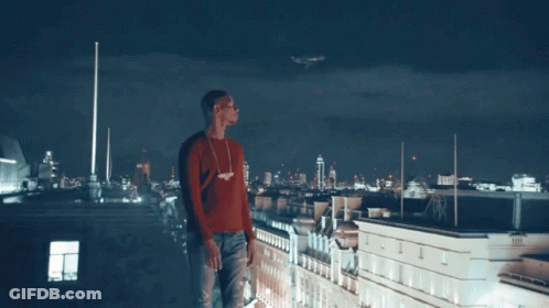 A Man In A Red Sweater Stands On The Roof Of A Building GIF