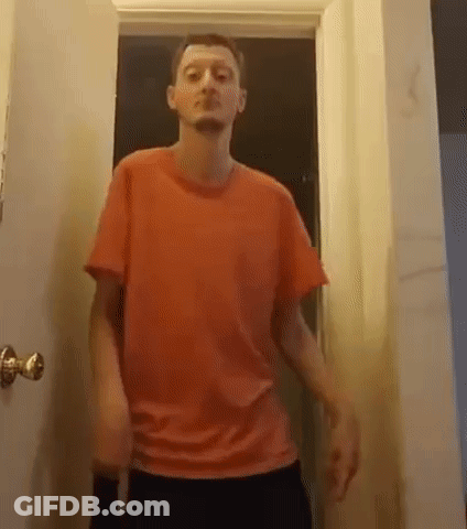 A Man In A Red T-Shirt Is Standing In A Doorway . GIF