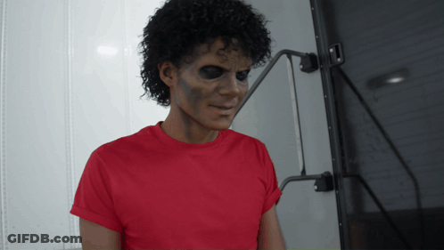 A Man In A Red T-Shirt Is Standing In Front Of A Wall GIF