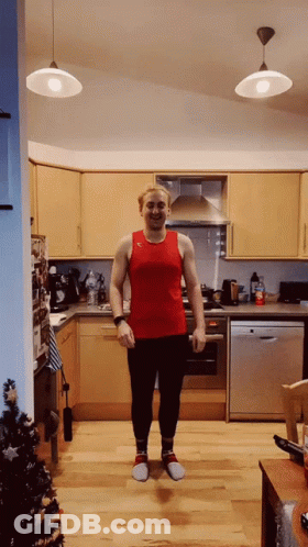 A Man In A Red Tank Top And Black Pants Is Standing In A Kitchen GIF