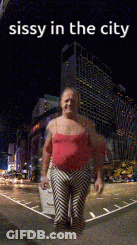 A Man In A Red Tank Top And Striped Pants Is Standing In Front Of A City At Night With The Caption Sissy In The City GIF