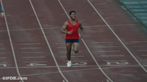 A Man In A Red Tank Top Is Running On A Track With His Arms Outstretched GIF