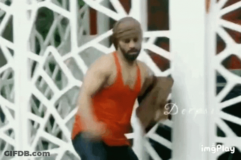 A Man In A Red Tank Top Is Standing In Front Of A White Fence . GIF