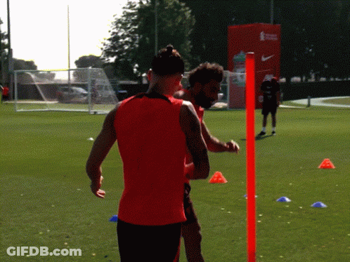 A Man In A Red Tank Top Is Standing Next To Another Man GIF