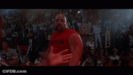 A Man In A Red Tank Top Is Standing Next To Another Man In A Wrestling Ring . GIF