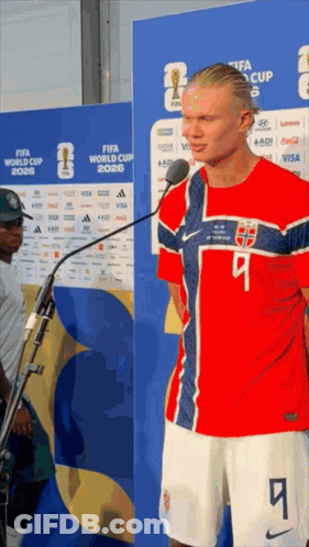 A Man In A Red White And Blue Jersey With The Number 9 On It Stands In Front Of A Microphone GIF