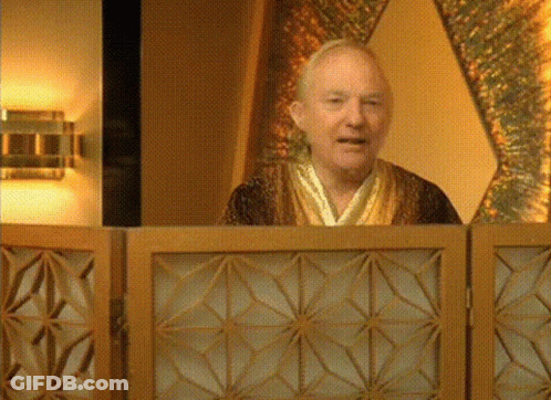 A Man In A Robe Is Behind A Wooden Screen And Smiling GIF