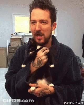 A Man In A Robe Is Holding A Black And White Cat In His Arms GIF