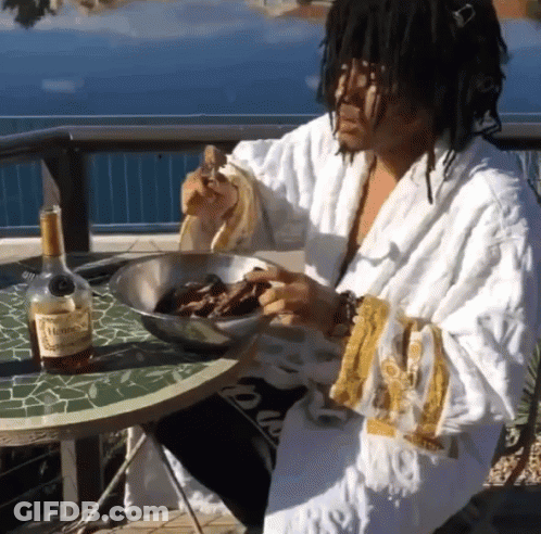 A Man In A Robe Is Sitting At A Table With A Bottle Of Hennessy GIF