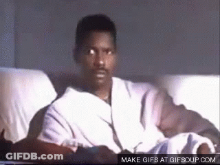 A Man In A Robe Is Sitting On A Couch And Looking At The Camera . GIF
