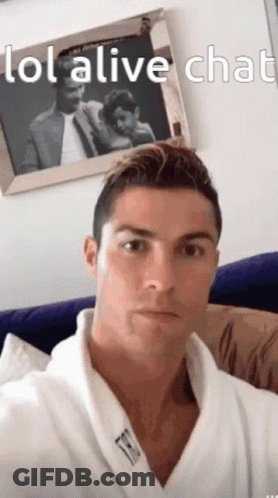 A Man In A Robe Is Sitting On A Couch In Front Of A Picture Of A Man And Woman . GIF