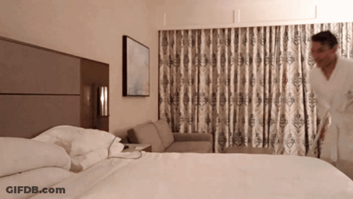 A Man In A Robe Is Standing In A Hotel Room GIF