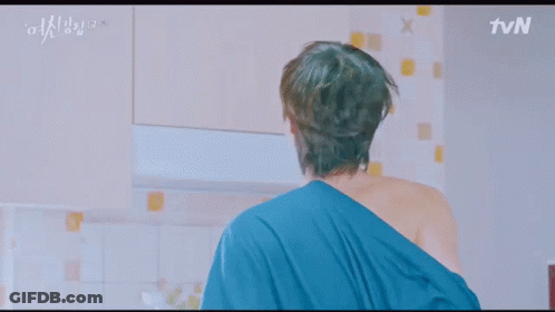 A Man In A Robe Is Standing In A Kitchen With A Microwave And A Refrigerator . GIF