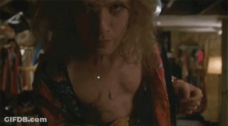 A Man In A Robe Is Standing In A Room With A Woman In A Blue Wig Behind Him . GIF