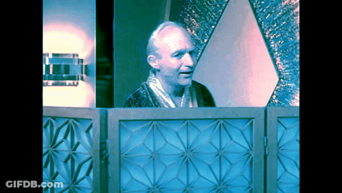A Man In A Robe Stands Behind A Blue Geometric Screen GIF