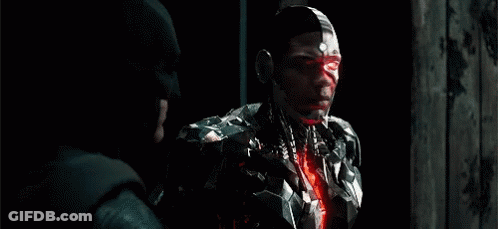 A Man In A Robotic Suit Is Standing Next To A Man In A Batman Hat . GIF