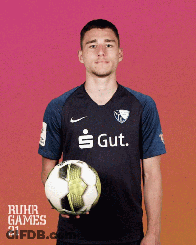 A Man In A Ruhr Games Shirt Holds A Soccer Ball In His Hands GIF