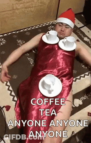 A Man In A Santa Hat Is Laying On The Floor With Cups Of Coffee On Plates Around His Waist . GIF