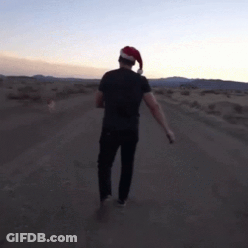 A Man In A Santa Hat Is Walking Down A Dirt Road GIF
