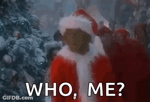 A Man In A Santa Suit Is Standing In Front Of A Christmas Tree And Asking Who Me . GIF