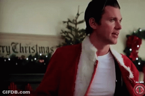 A Man In A Santa Suit Is Standing In Front Of A Sign That Says " Merry Christmas " GIF